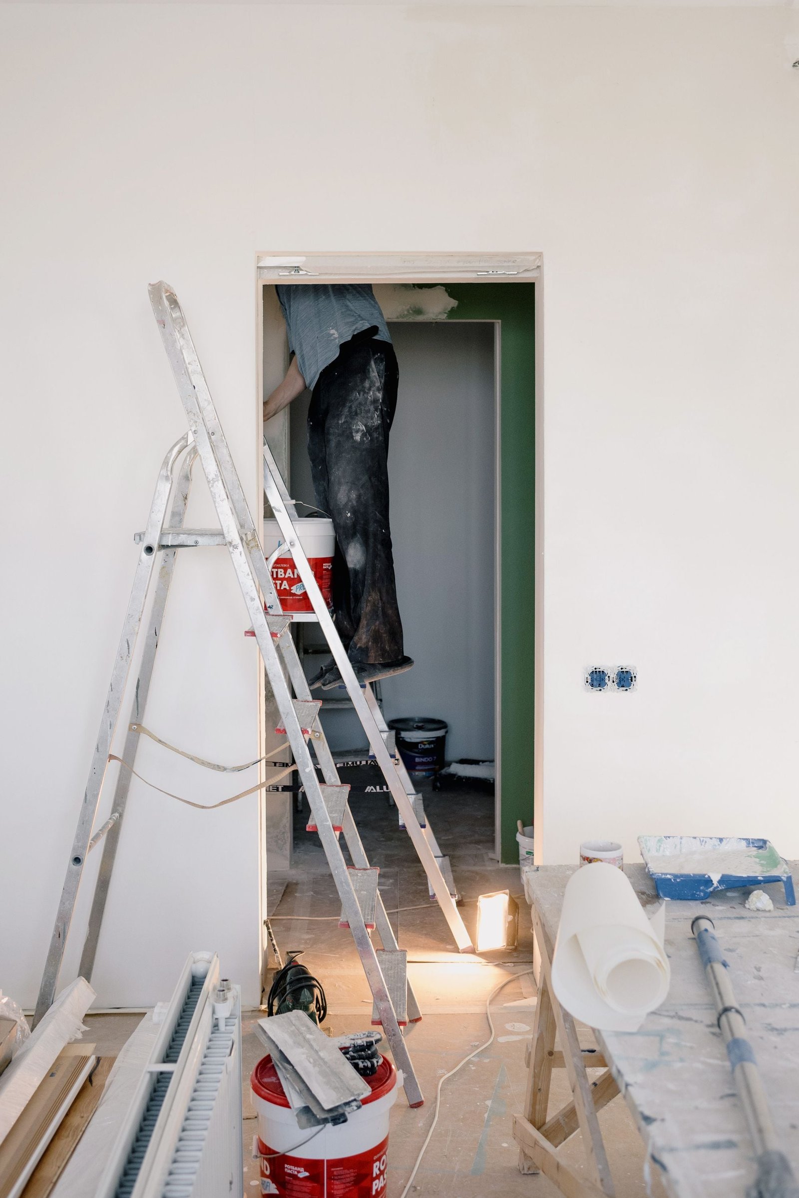 Een ladder en een verfemmer in een kamer waar wordt geschilderd
